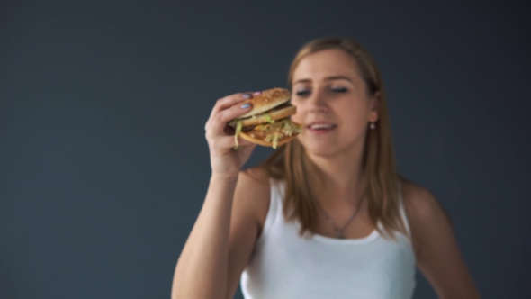 Overweight Woman with a Hamburger on a Gray Background alt