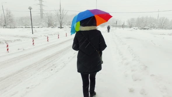 Girl Goes Under a Multi-colored Umbrella in Heavy Snow