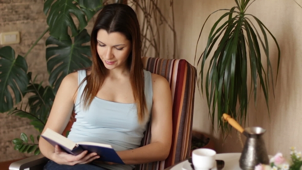 Young Attractive Woman Reading Interesting Book While Sitting on Comfortable Chair in the Living