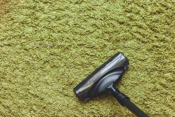 The head of a vacuum cleaner brush on the green carpet, the top view. Stock Photo by Vladdeep