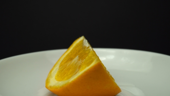 A Piece of Fresh Orange Fruit Is Zooming and Rotating on the White Plate.
