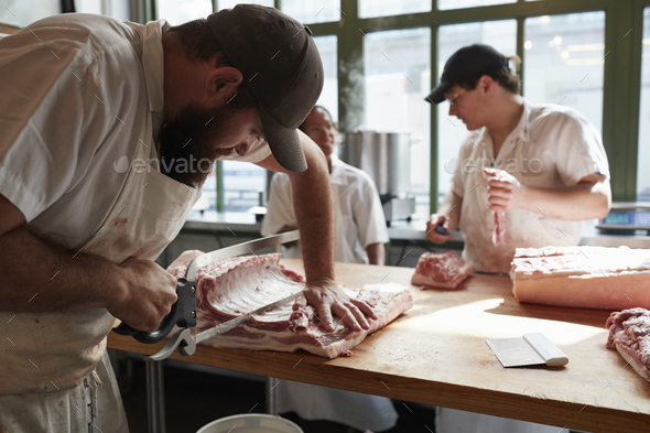 Three butchers preparing meat,cuts of meat in butcher's shop, close up Stock Photo by monkeybusiness