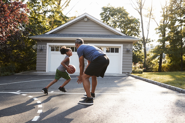 Father And Son Playing Basketball On Driveway At Home Stock Photo by monkeybusiness