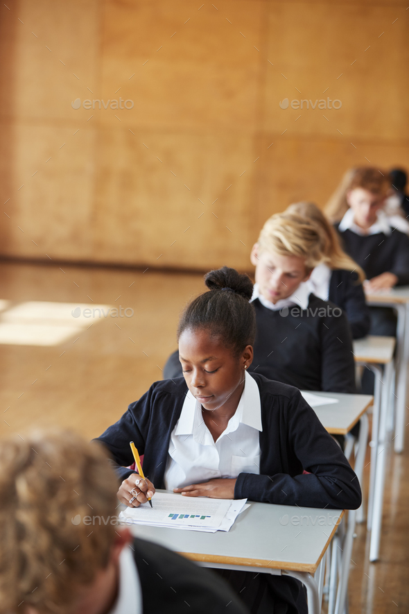 Teenage Students In Uniform Sitting Examination In School Hall Stock Photo by monkeybusiness