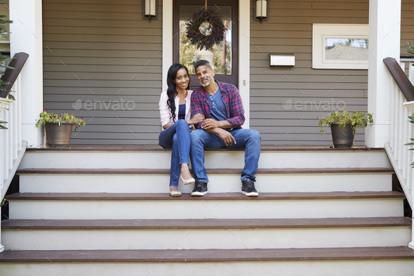 Couple Sitting On Steps Leading Up To Porch Of Home Stock Photo by monkeybusiness