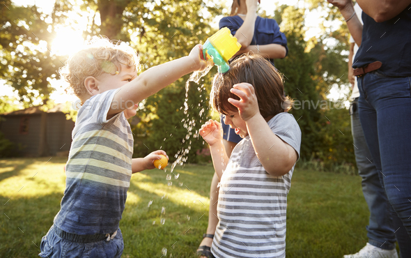 Boy Pouring Water Over Friends Head In Garden Stock Photo by monkeybusiness