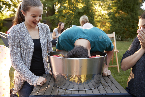 Friends watch teenage boy apple bobbing at a garden party - Stock Photo - Images