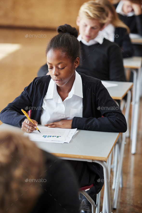 Teenage Students In Uniform Sitting Examination In School Hall Stock Photo by monkeybusiness