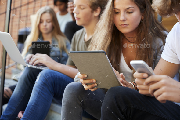 Teenage Students Using Digital Devices On College Campus Stock Photo by monkeybusiness