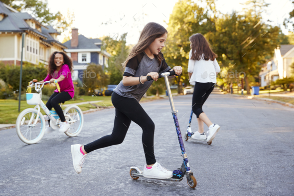 Girls playing in the street on scooters and a bike, close up Stock Photo by monkeybusiness