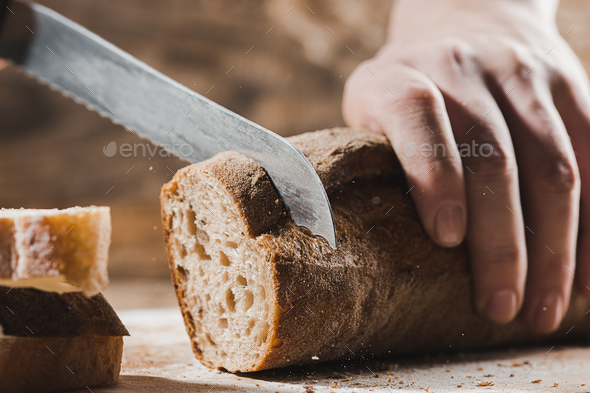 Whole grain bread put on kitchen wood plate with a chef holding gold knife for cut. Stock Photo by master1305