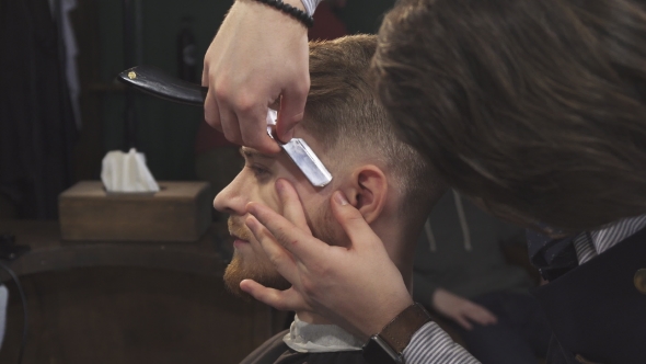 of a Handsome Man Getting Shaved with a Razor By a Barber alt