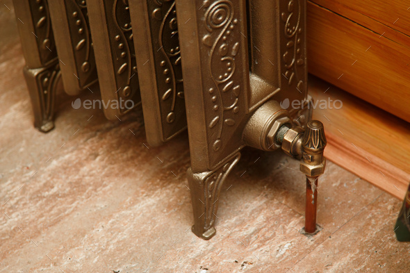 Retro styled cast iron radiator with valve and copper pipe. Close up Stock Photo by Vladdeep
