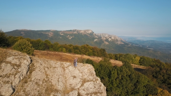 Aerial Flight Over Young Couple Standing on Cliff Edge  alt