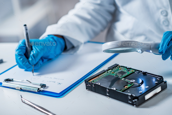 Forensic science expert examining hard drive Stock Photo by microgen