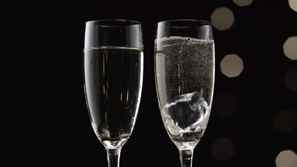 Two Flutes of Champagne with Transparent Pieces of Ice on the bottom Bokeh Blinking Black Background alt