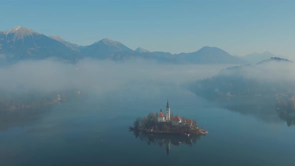 Revealing shot of Lake Bled, Slovenia, on a beautiful foggy morning in Spring. alt