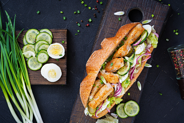 Baguette sandwich with fish, egg, pickled onions and lettuce leaves. Top view Stock Photo by Timolina