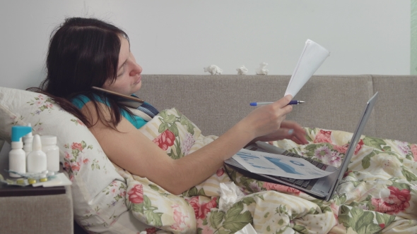 Sick Woman Lying in Bed at Home, Talking on the Phone and Working on Laptop alt