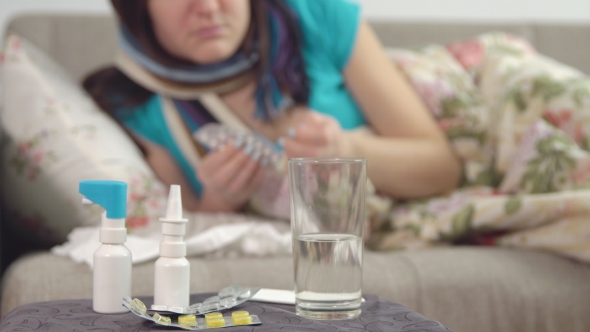 Tablets, Spray and Water on the Chair and Young Sick Woman Takes a Pill alt