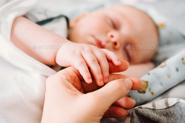 Cute newborn baby holding mother\'s hand while sleeping. Happy Family concept. Stock Photo by Determined