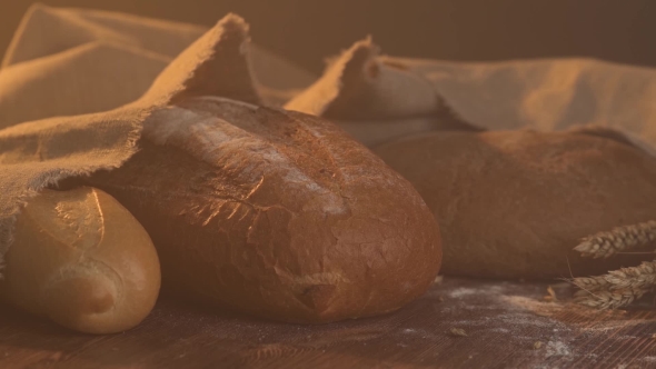 Handmade Tasty Bread Lying on Burlap on the Wooden Table with Flour, Wheat and Ears of Wheat
