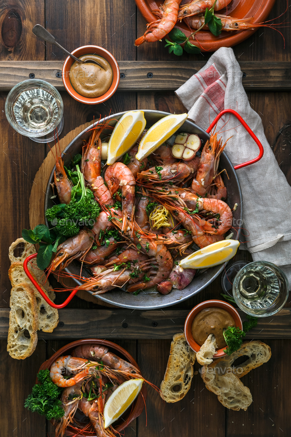 Paella pan with roasted tiger prawns and many dishes, bread and wine Stock Photo by fazeful
