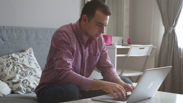 A Person Works From Home Using the Top and Trackpad. Young Business Man Sitting at Table Drinking alt