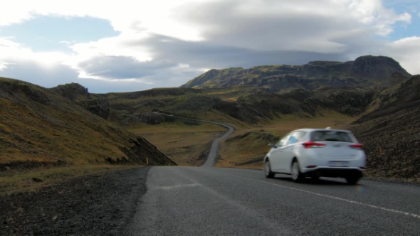 White Car Is Moving over Road Between Picturesque Icelandic Mountains in Cloudy Weather