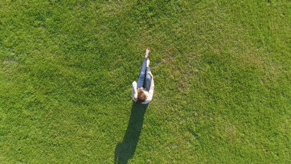 Aerial View. Young Girl Lying and Resting on Lawn on Sunny Day in Park on Grass. Above View. Woman
