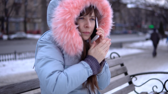 A Young Woman in a Gray Warm Jacket Uses a Phone in the Street in the Winter alt