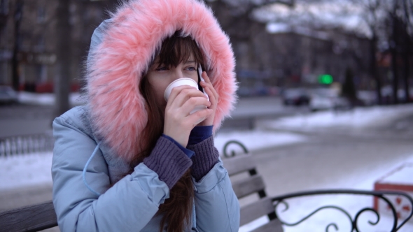 A Young Woman in a Gray Warm Jacket Uses a Phone in the Street in the Winter. alt