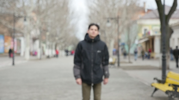 A Sportive Young Man in a Black Parka Strolls in an Alley in Winter in