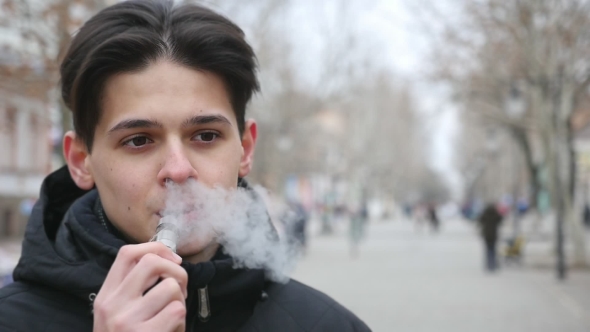 A Handsome Man Stands Outdoors and Smokes an E-cigarette in Winter