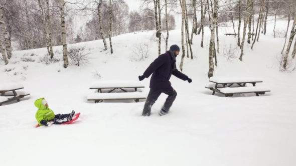 Father Pulling Red Bobsled on Snowy Field with child.Dad, Son or Daughter alt