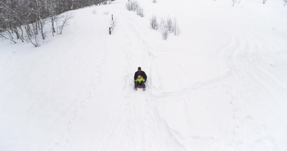 Winter Aerial  Follow Father Riding Red Bobsled on Snowy Downhill with Child.Dad, Son or Daughter alt