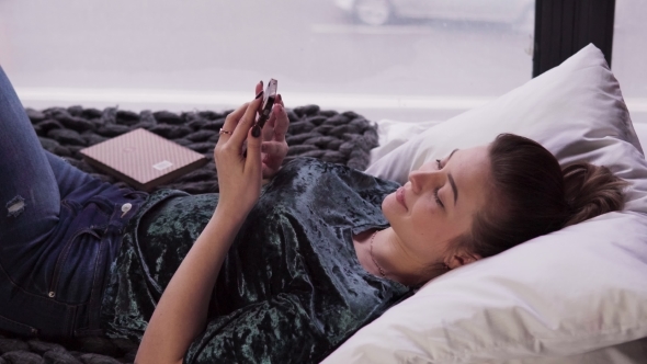Young Female Using Smartphone on Bed By Window