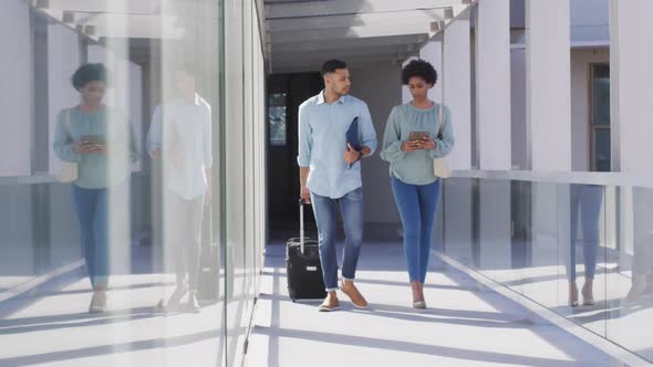 Video of diverse businessman and businesswoman walking with suitcase and talking alt