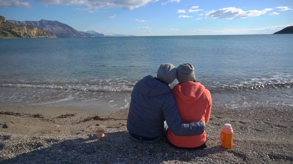 Back View of Romantic Couple Sitting on the Beach and Look at the Sea