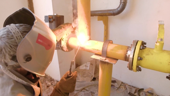 Welder Is Welding Big Yellow Pipes Inside a Maintainable Space, Using Welding Machine, Protective alt