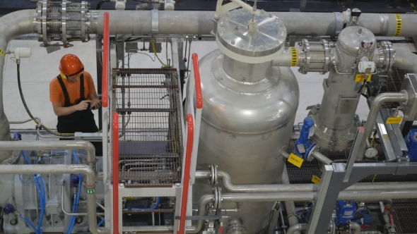 Engineer Looking at the High Pressure Air Compressor and Controls the Readings on the Smartphone. alt