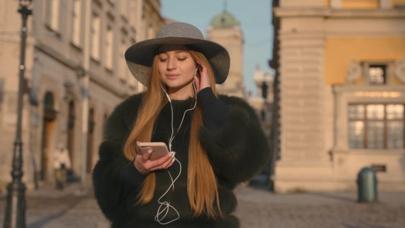 Young Woman in a Gray Hat and Long Hair Communicates Via Smartphone alt