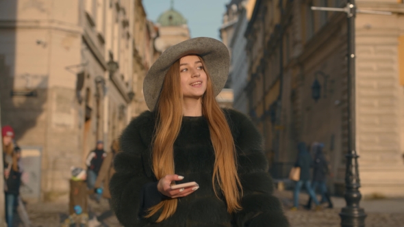 Young Woman in a Gray Hat and Long Hair Communicates Via Smartphone alt