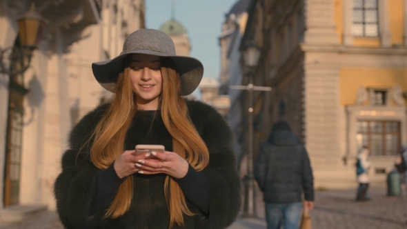 Young Woman in a Gray Hat and Long Hair Communicates Via Smartphone alt