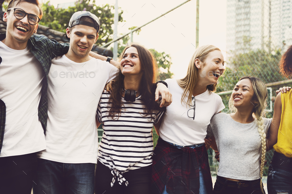 Smiling happy young adult friends arms around shoulder outdoors