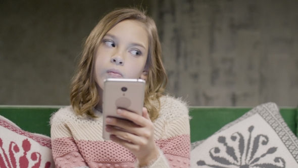 Young Girl Holding Phone in Hands Sitting in Room alt