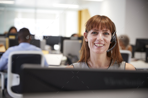 Young woman working at computer with headset in busy office Stock Photo by monkeybusiness