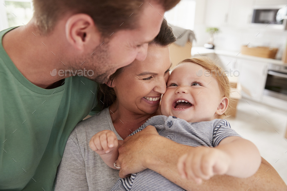 Close Up Of Parents Hugging Happy Baby Son At Home Stock Photo by monkeybusiness