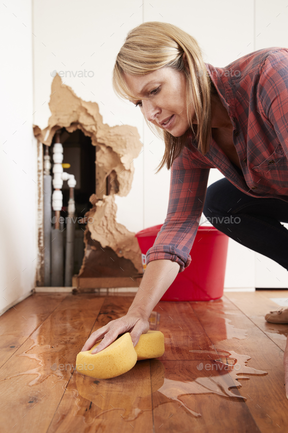 Woman mopping up water from a burst pipe with sponge, vertical Stock Photo by monkeybusiness