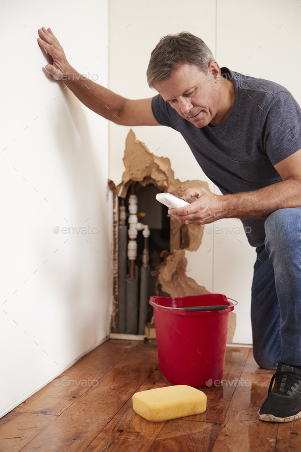 Middle aged man with a burst pipe dialling phone for help Stock Photo by monkeybusiness